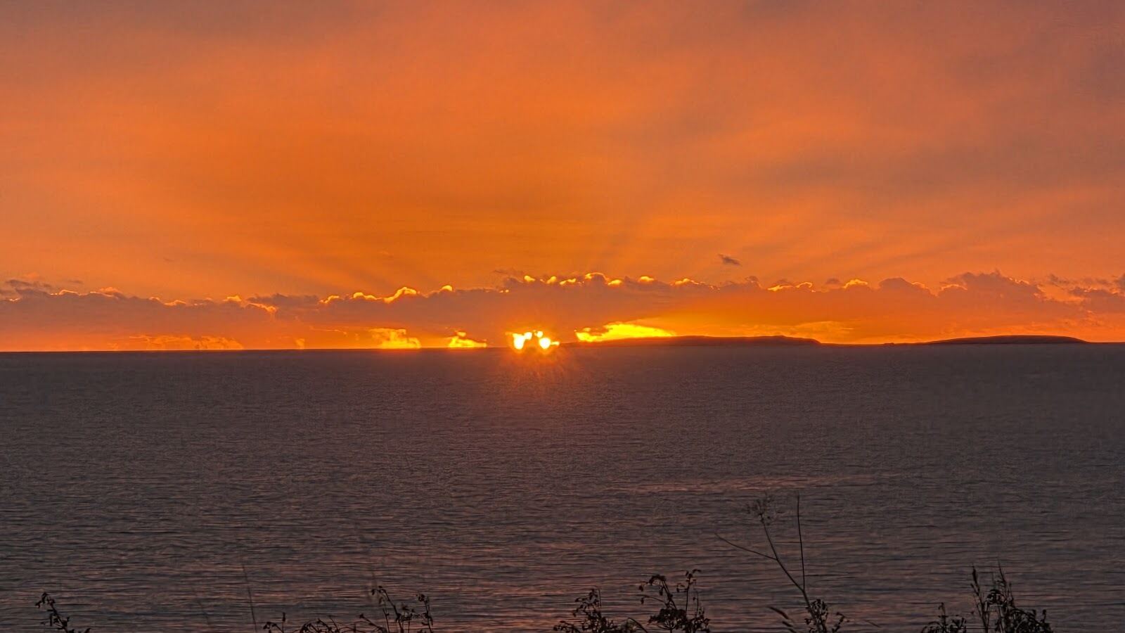 Sunset over the sea, with the sun low on the horizon and an orange sky